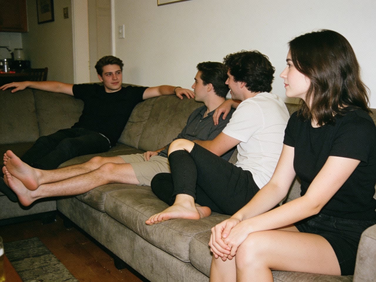 Five friends along a sofa at a house party; four are sprawled out taking up room, while one perches on the front edge of the cushion with her arms against her sides and both hands held together in her lap.